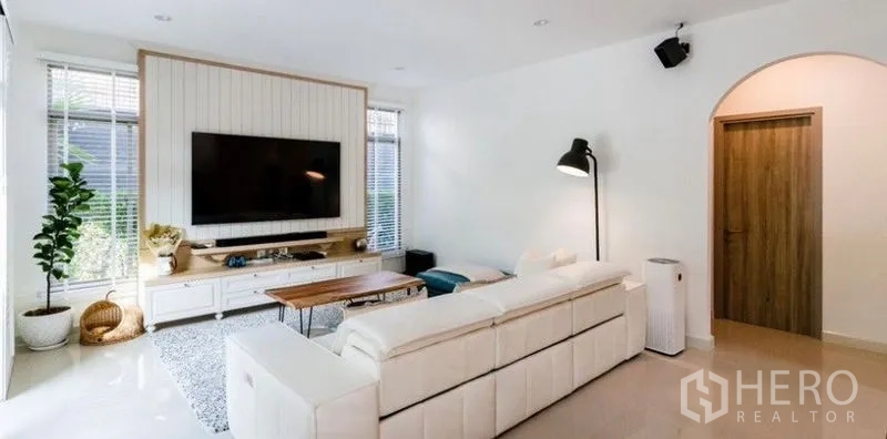 Detached House for rent - Cozy living room featuring a wall-mounted TV, white media cabinet, sectional sofa, and indoor plant.