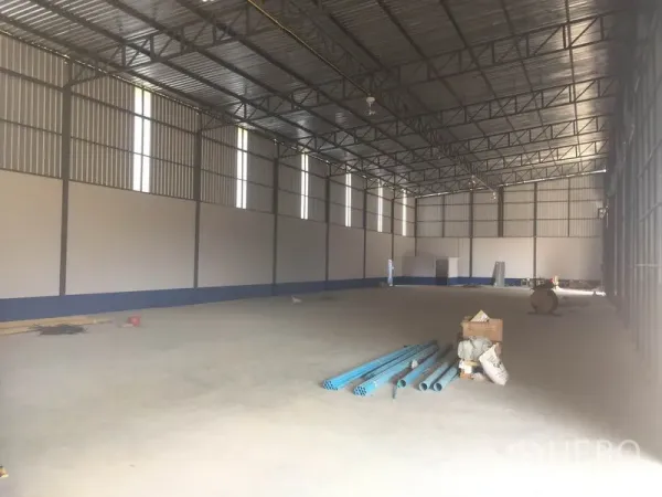 Warehouse for rent in Sai Mai, Bangkok - Spacious open warehouse floor with concrete slab, long-span trusses and natural light, materials on the ground.