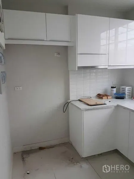 Townhouse for rent in Bang Na, Bangkok - Compact white L-shaped kitchen with glossy cabinets, tiled backsplash and overhead storage.