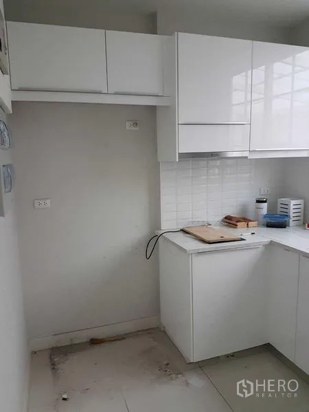 Townhouse for rent in Bang Na, Bangkok - Compact white L-shaped kitchen with glossy cabinets, tiled backsplash and overhead storage.