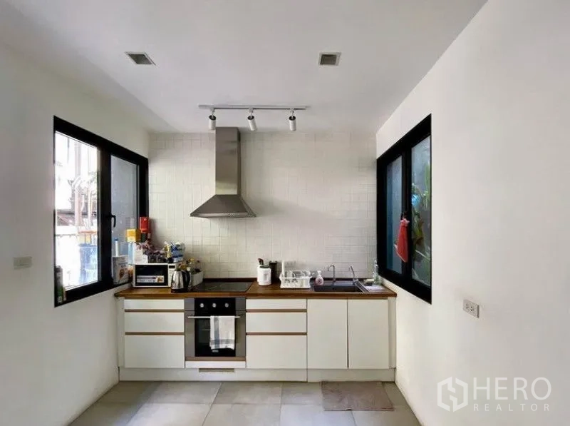 Townhouse for rent in Khlong Toei, Bangkok - Bright white kitchen with built-in cabinets, oven, range hood and dual windows.