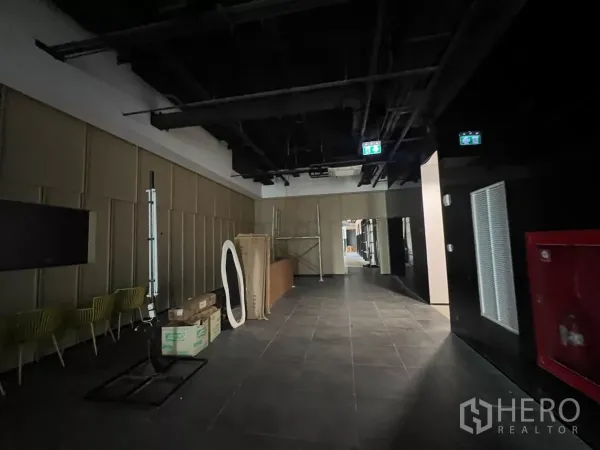 Retail Space for rent - Common area lobby with dark tiled flooring, exposed ceiling services and emergency exit signs.