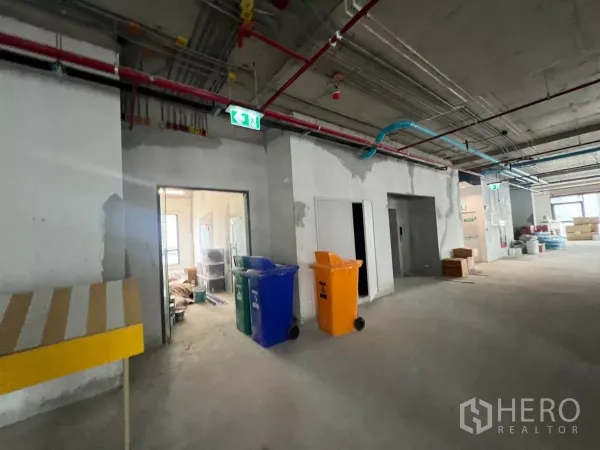 Office Space for rent in Khlong Toei, Bangkok - Core-and-shell office corridor showing exposed MEP lines, exit signage and service rooms.