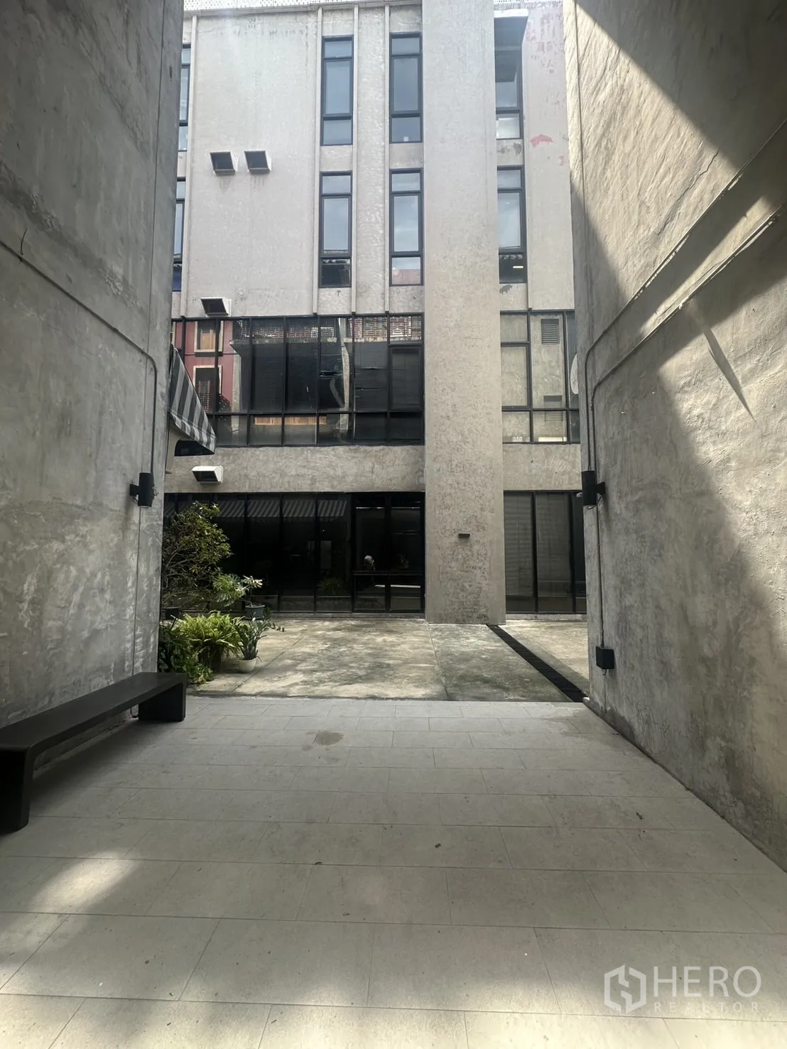 Home Office for rent in Pathum Wan, Bangkok - Shared courtyard between buildings with bench, greenery and concrete walkways.