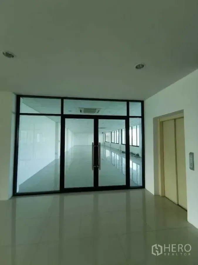 办公空间 出租 - 玻璃双开门办公室入口，旁连电梯大堂，瓷砖地面与黑色铝框，空间明亮。