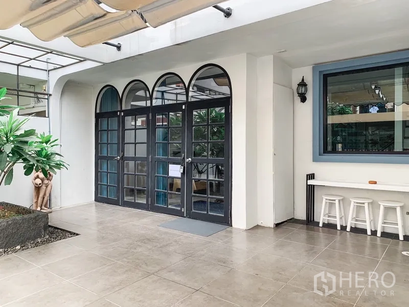 Townhouse for rent in Watthana, Bangkok - Townhouse entrance featuring arched black-framed glass doors and a tiled patio.