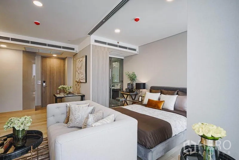 Condominium for sale in Khlong Toei, Bangkok - Open-plan bedroom and living area with tufted sofa, double bed, desk and a glass-walled bathroom.