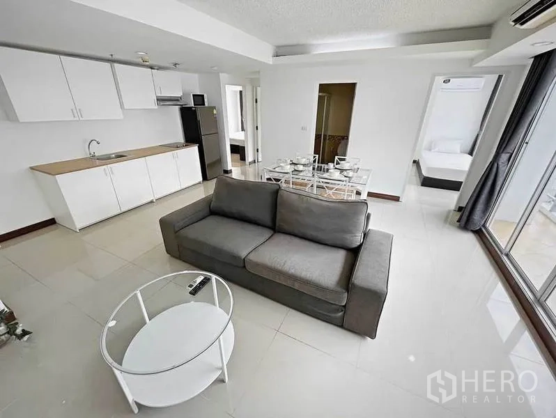 Condominium for rent in Khlong Toei, Bangkok - Living space perspective showing kitchen, dining table, gray sofa and full-height windows.