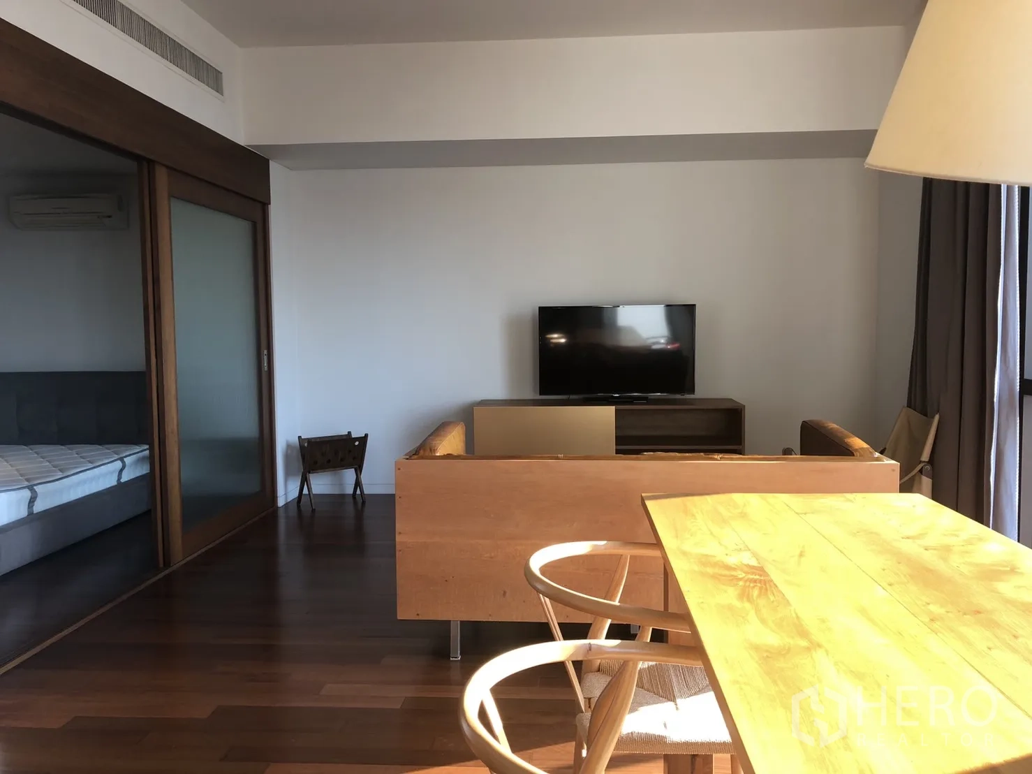 Condominium for rent in Pathum Wan, Bangkok - Living area facing a TV with wooden dining set and a sliding door leading into the bedroom.