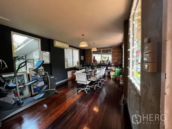 Townhouse for rent - Open-plan room with dark wood floors, meeting table, large windows and exercise equipment.