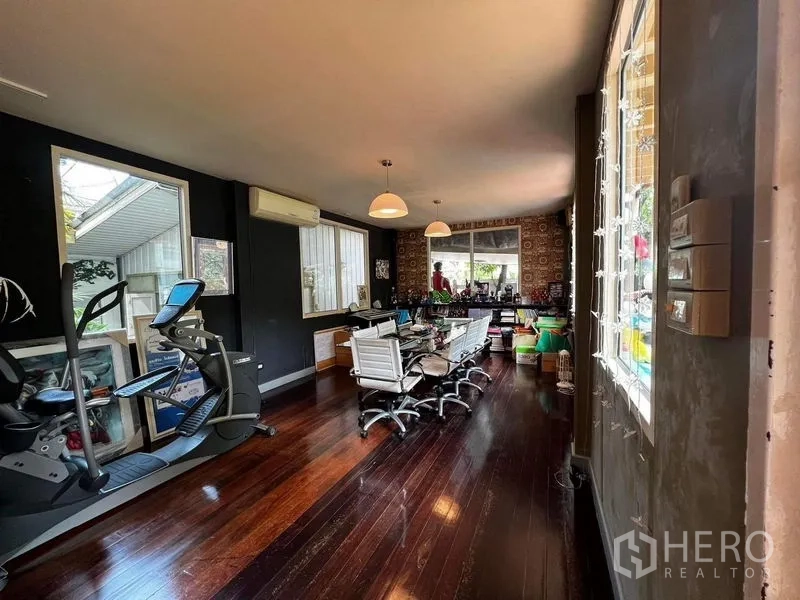 Townhouse for rent - Open-plan room with dark wood floors, meeting table, large windows and exercise equipment.