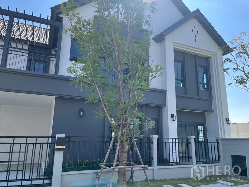 Detached House for rent in Bang Phli, Samut Prakan - Modern two-storey detached house facade in Bang Phli with grey-white exterior, fenced yard and young tree.
