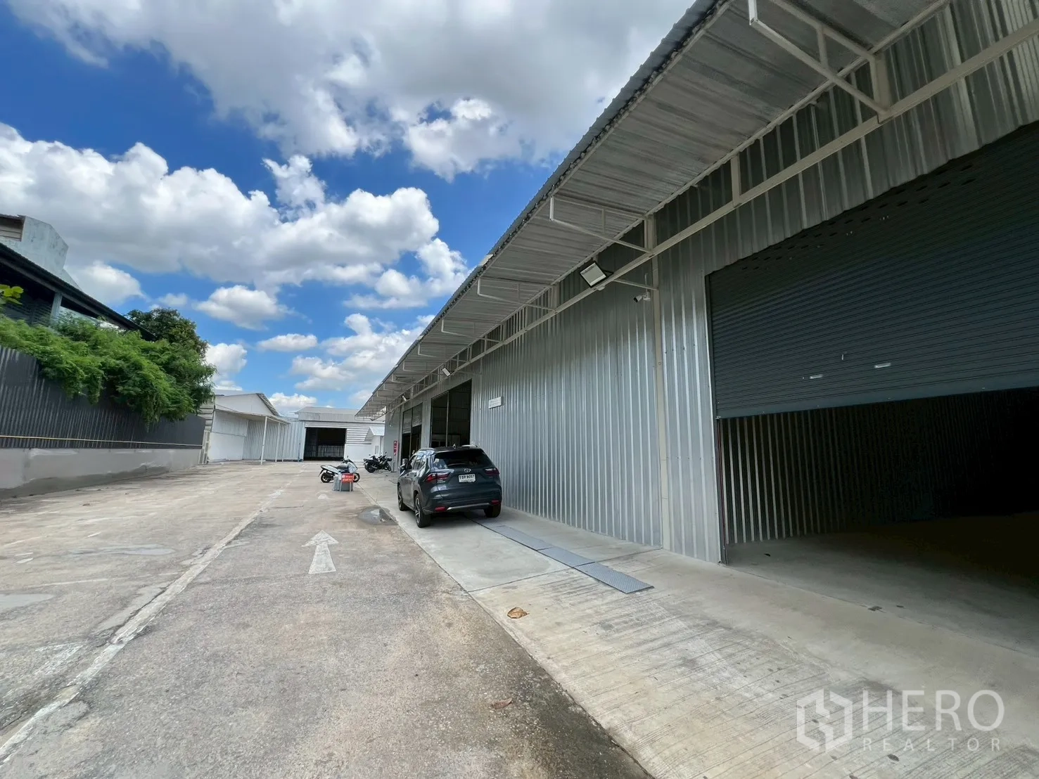 Warehouse for rent in Min Buri, Bangkok - Exterior of warehouse bays with car parking and a wide access road suitable for trucks.