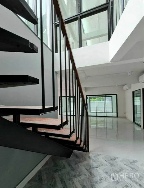 Home Office for rent in Lat Phrao, Bangkok - Close-up of the airy atrium and staircase beside full-height glass panels.