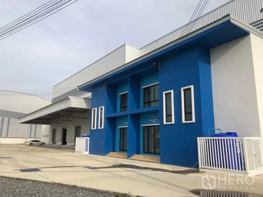 工厂 出租在Samut Prakan - 北榄府邦沙通工厂外观，蓝色两层办公楼，宽阔车道及带顶装卸区。