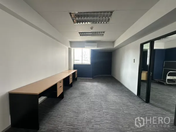 Office Space for rent in Watthana, Bangkok - Private work area with long built-in desks, grey carpet and ceiling grid lights beside a window.