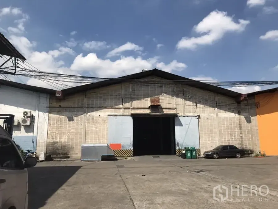 Warehouse for rent in Khlong Toei, Bangkok - Front of a gable‑roof warehouse with large sliding doors and spacious vehicle access.
