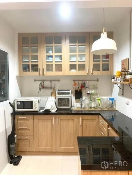 Townhouse for rent in Suan Luang, Bangkok - Compact built-in kitchen with wood cabinets, black granite countertop and pendant light.