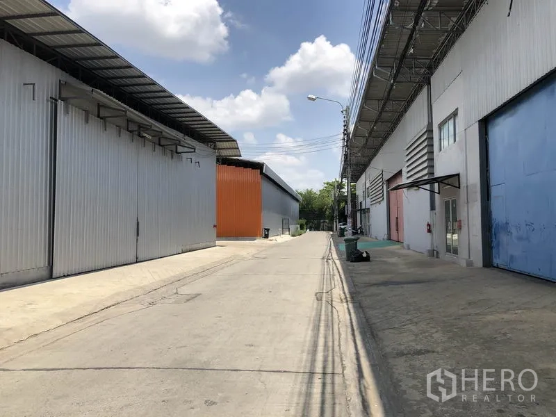 Warehouse for rent in Bang Kapi, Bangkok - Wide access road between warehouse buildings with covered eaves and multiple roller doors suitable for truck entry.