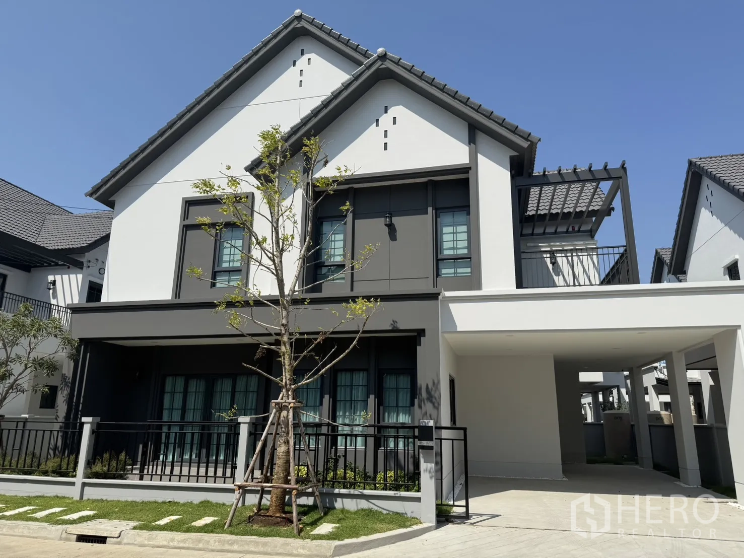独立式住宅 for rent in Bang Phli, Samut Prakan - 现代两层独栋别墅外立面，带车棚、阳台平台、草坪与围栏。