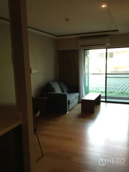 Condominium for rent in Khlong Toei, Bangkok - Living area with wood flooring, sofa and sliding glass door opening to a balcony.