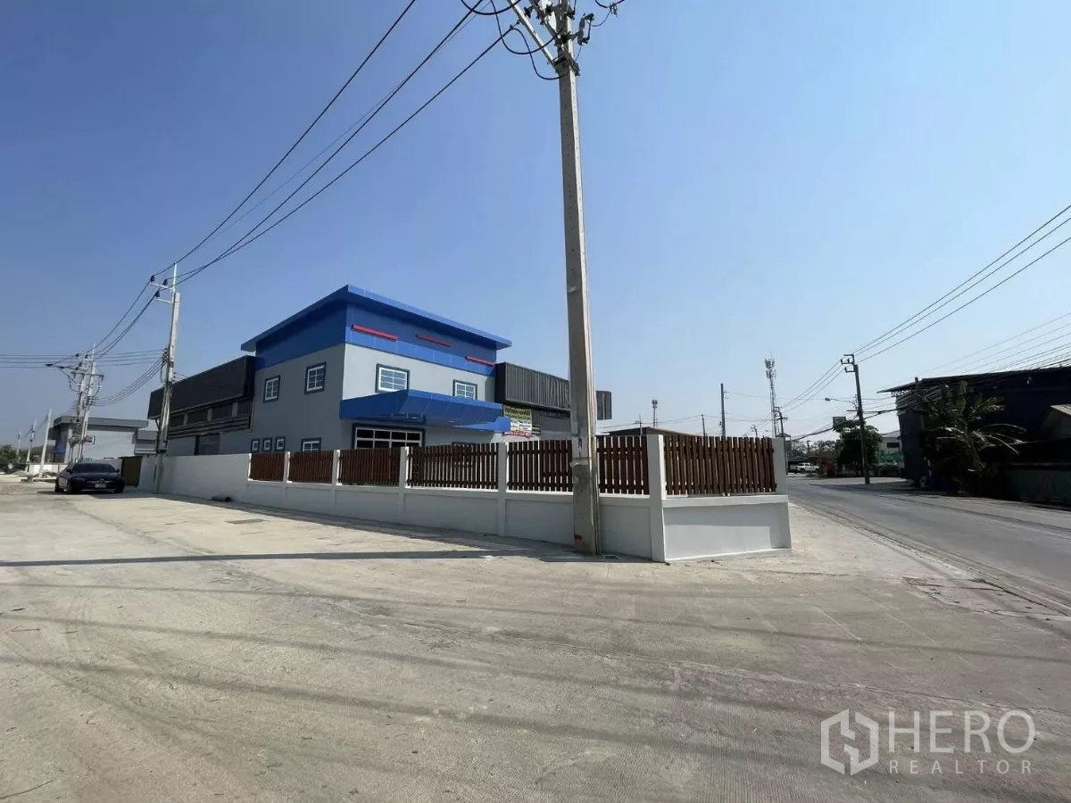 Factory for rent or sale in Bang Phli, Samut Prakan - Corner exterior perspective showing boundary wall, wooden fencing, and direct road access.