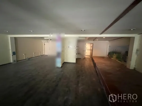 Shophouse for rent in Watthana, Bangkok - Spacious ground-floor retail area with dark flooring, recessed lights and a raised platform.