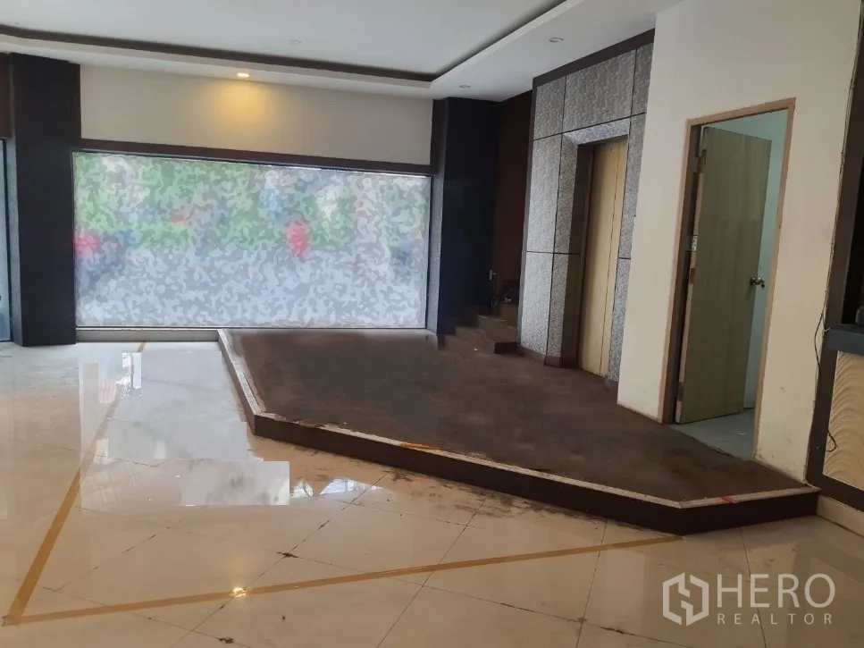 店屋 出租在Khlong Toei, Bangkok - 一层临街空间，设大幅磨砂展示窗、抬高平台、电梯入口与亮面瓷砖地面。