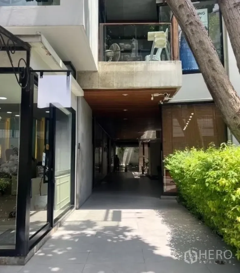 Retail Space for rent in Watthana, Bangkok - Shaded retail passage with modern glass storefronts, wooden soffit ceiling, and a hedge-lined walkway.