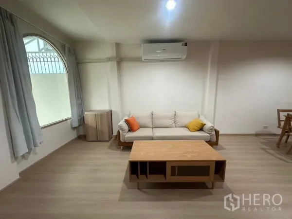 Townhouse for rent or sale in Phra Khanong, Bangkok - Cozy living corner with sofa, arched window and air-conditioning.