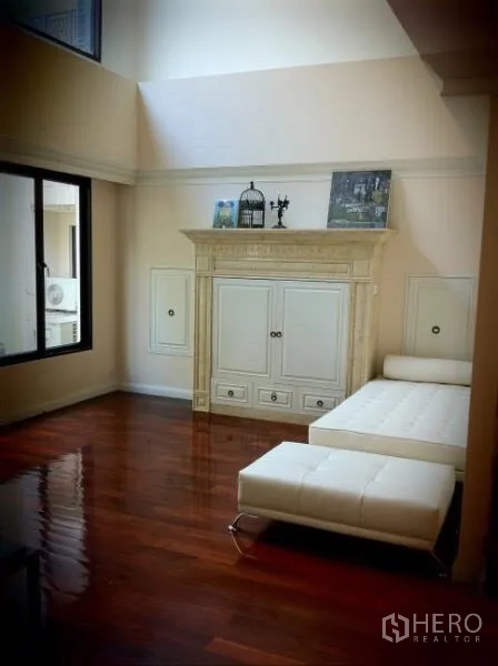 Townhouse for rent in Khlong Toei, Bangkok - Upper-floor lounge with polished wood floors, classic cabinet feature and white chaise.