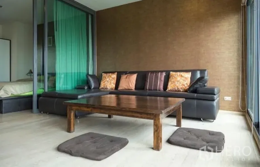 Condominium for rent in Khlong Toei, Bangkok - Bright living room with leather sectional sofa, wooden coffee table, and large windows.