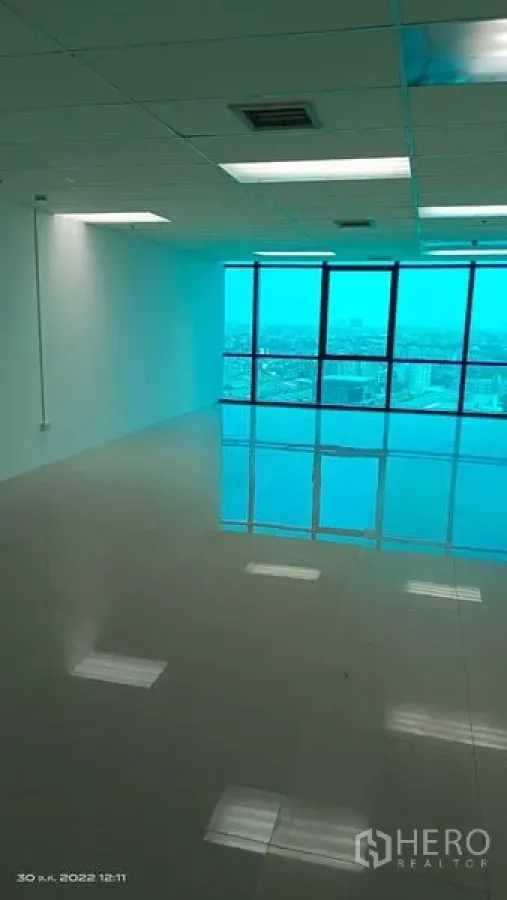 办公空间 出租在Huai Khwang, Bangkok - 空旷开放式办公室，亮面地砖、吊顶灯，蓝色落地窗俯瞰曼谷城市天际线。