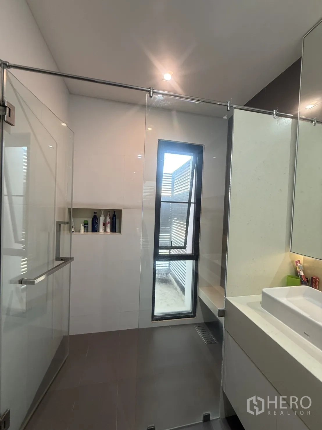 Detached House for rent in Bang Kapi, Bangkok - Bright bathroom with glass-enclosed shower, window, and toiletry niche.