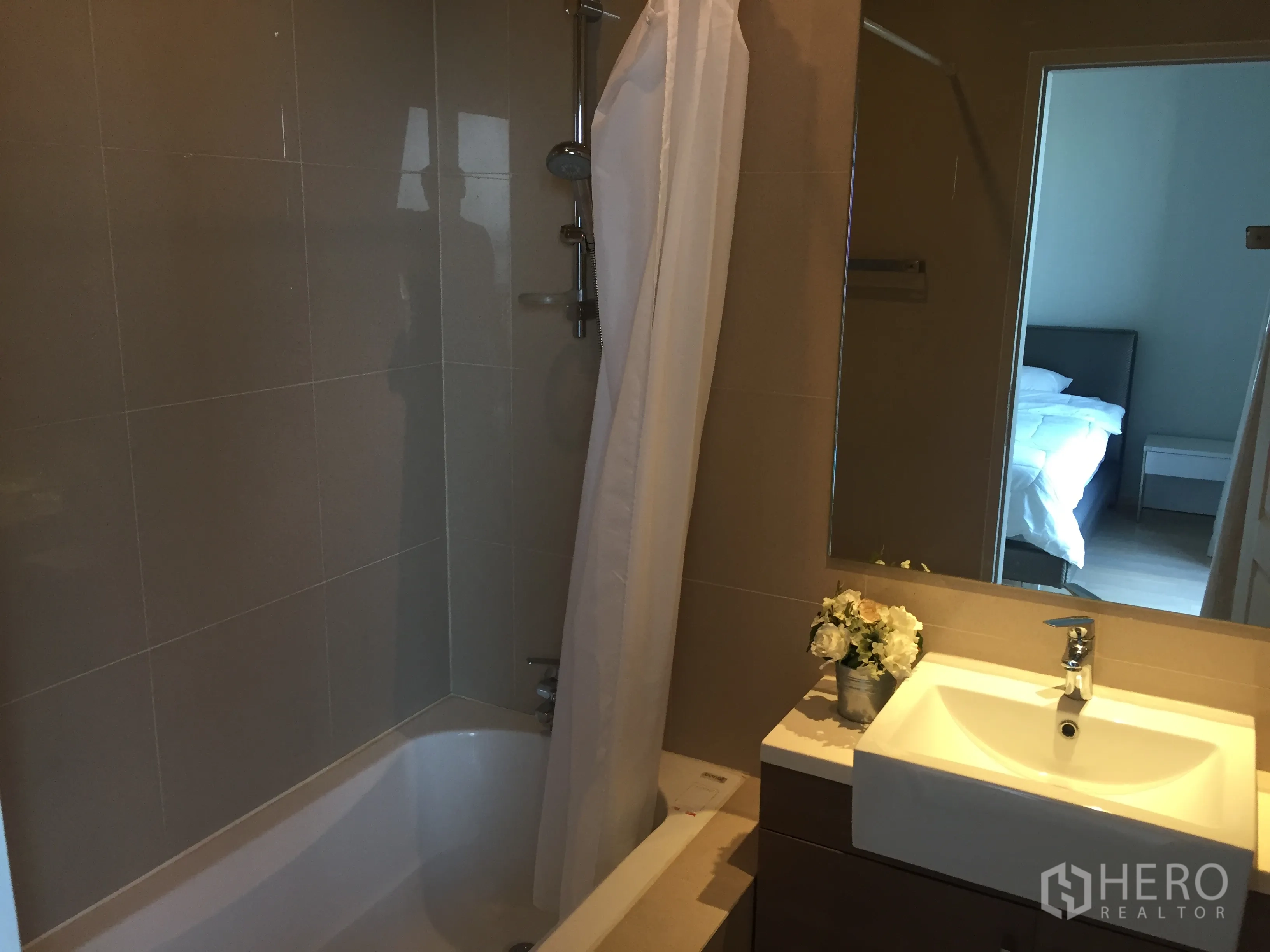 Condominium for rent in Bangkok - Modern bathroom with bathtub and shower combo, vanity, and large mirror.