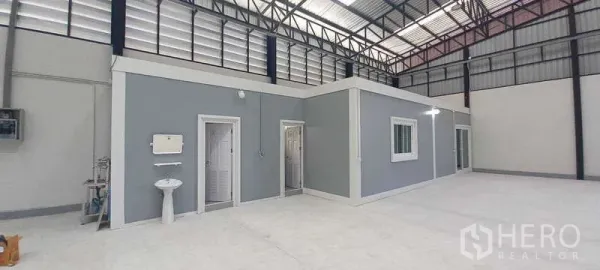 Warehouse for rent or sale in Khlong Luang, Pathum Thani - Interior of a high-clearance warehouse with a built-in grey office block, restrooms, windows and polished concrete floor.