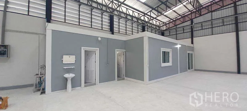 Warehouse for rent or sale in Khlong Luang, Pathum Thani - Interior of a high-clearance warehouse with a built-in grey office block, restrooms, windows and polished concrete floor.