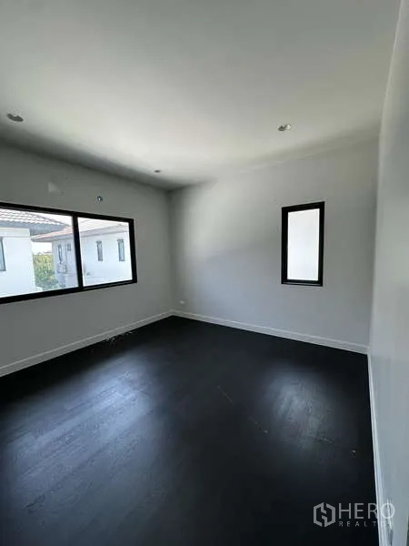 Detached House for sale in Lam Luk Ka, Pathum Thani - Bright bedroom with two windows and dark wood flooring.