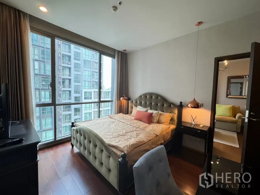 Condominium for rent in Watthana, Bangkok - Bright bedroom with tufted bed, pendant light and large window facing nearby towers.