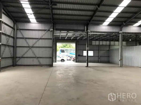 货栈 出租在Pak Kret, Nonthaburi - 面向大卷闸装卸门的开阔库区，外部可见停放车辆。