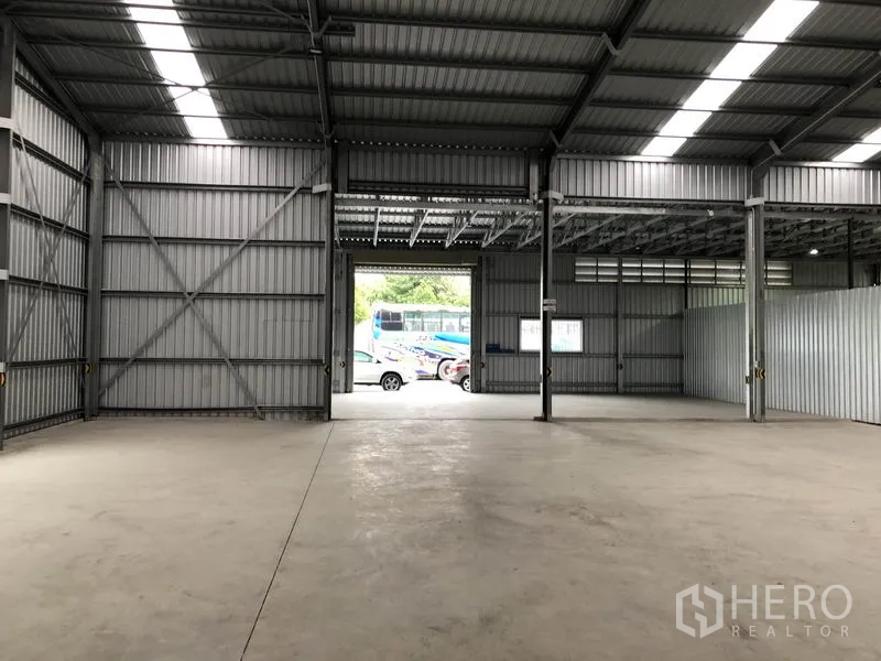 货栈 出租在Pak Kret, Nonthaburi - 面向大卷闸装卸门的开阔库区，外部可见停放车辆。
