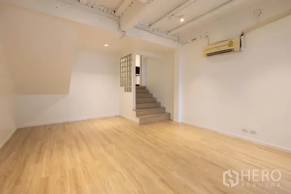 Townhouse for rent in Khlong Toei, Bangkok - Open living area with timber floors, ceiling spotlights and short steps leading to a raised section.
