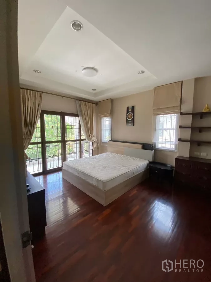 Detached House for rent or sale in Mueang Nonthaburi, Nonthaburi - Master bedroom with wooden flooring, balcony doors and large curtained windows.