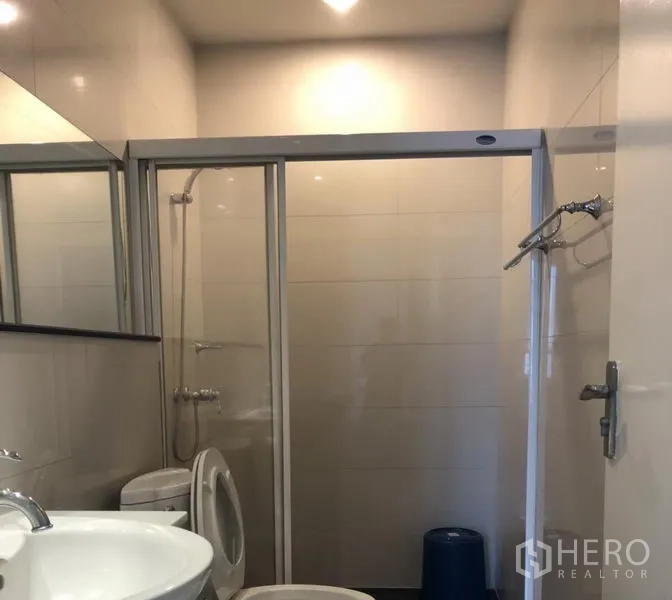 Condominium for rent in Pathum Wan, Bangkok - Bathroom featuring a sliding-glass shower enclosure, vanity, and an in-unit washing machine.