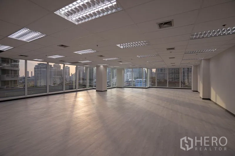 Office Space for rent in Bang Rak, Bangkok - Open-plan office at dusk with panoramic glazing and warm natural light across wood-look floors.