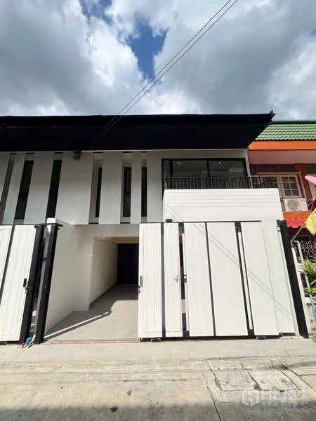 Townhouse for sale in Khlong Toei, Bangkok - Modern two-storey townhouse exterior with white facade, gated parking and a small balcony in Phra Khanong.