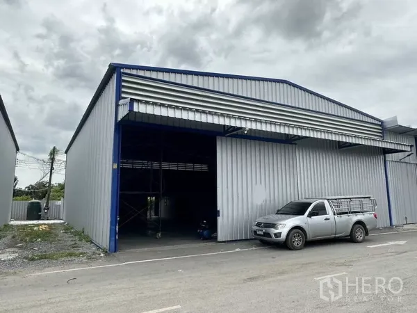 Warehouse for rent in Khlong Luang, Pathum Thani - Close-up of gable-roof warehouse facade with large shutter opening and pickup truck at the loading area.