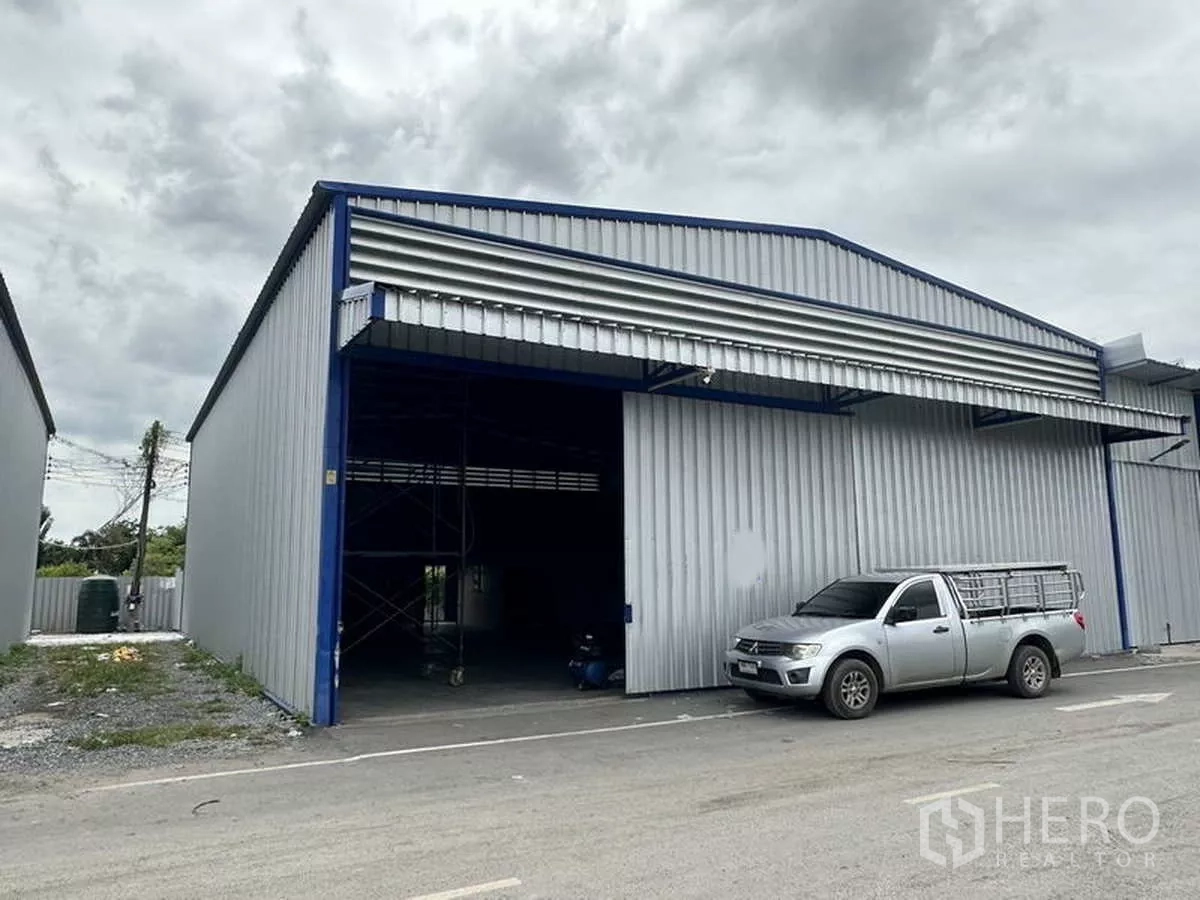 Warehouse for rent in Khlong Luang, Pathum Thani - Close-up of gable-roof warehouse facade with large shutter opening and pickup truck at the loading area.