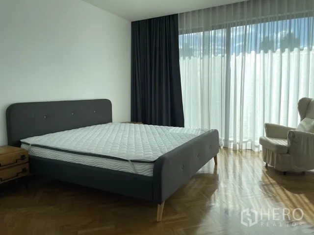 Detached House for rent in Watthana, Bangkok - Primary bedroom with gray bed, armchair, and long sheer curtains.