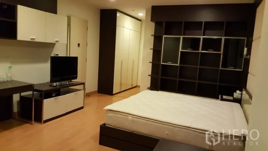 Condominium for rent in Khlong Toei, Bangkok - Spacious bedroom with built-in shelving wall, TV console, wardrobes and wood flooring.